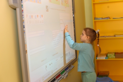 Uczennica rozwiązuje zadania matematyczne na interaktywnej tablicy.