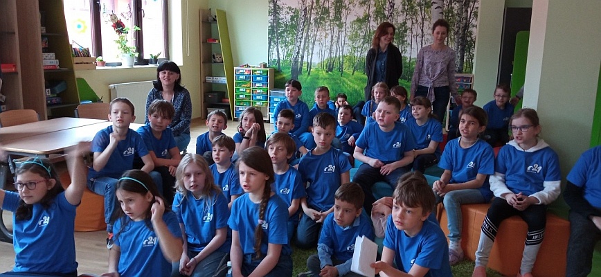 Wspólne zdjęcie uczniów ubranych w niebieskie koszlki na szkolnej świetlicy.