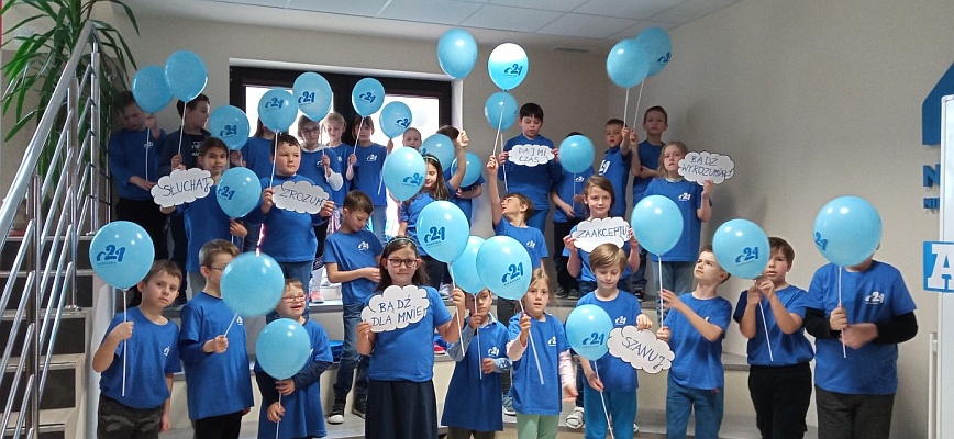 Ubrani na niebiesko uczniowie wraz z niebieskimi balonikami na holu szkoły.